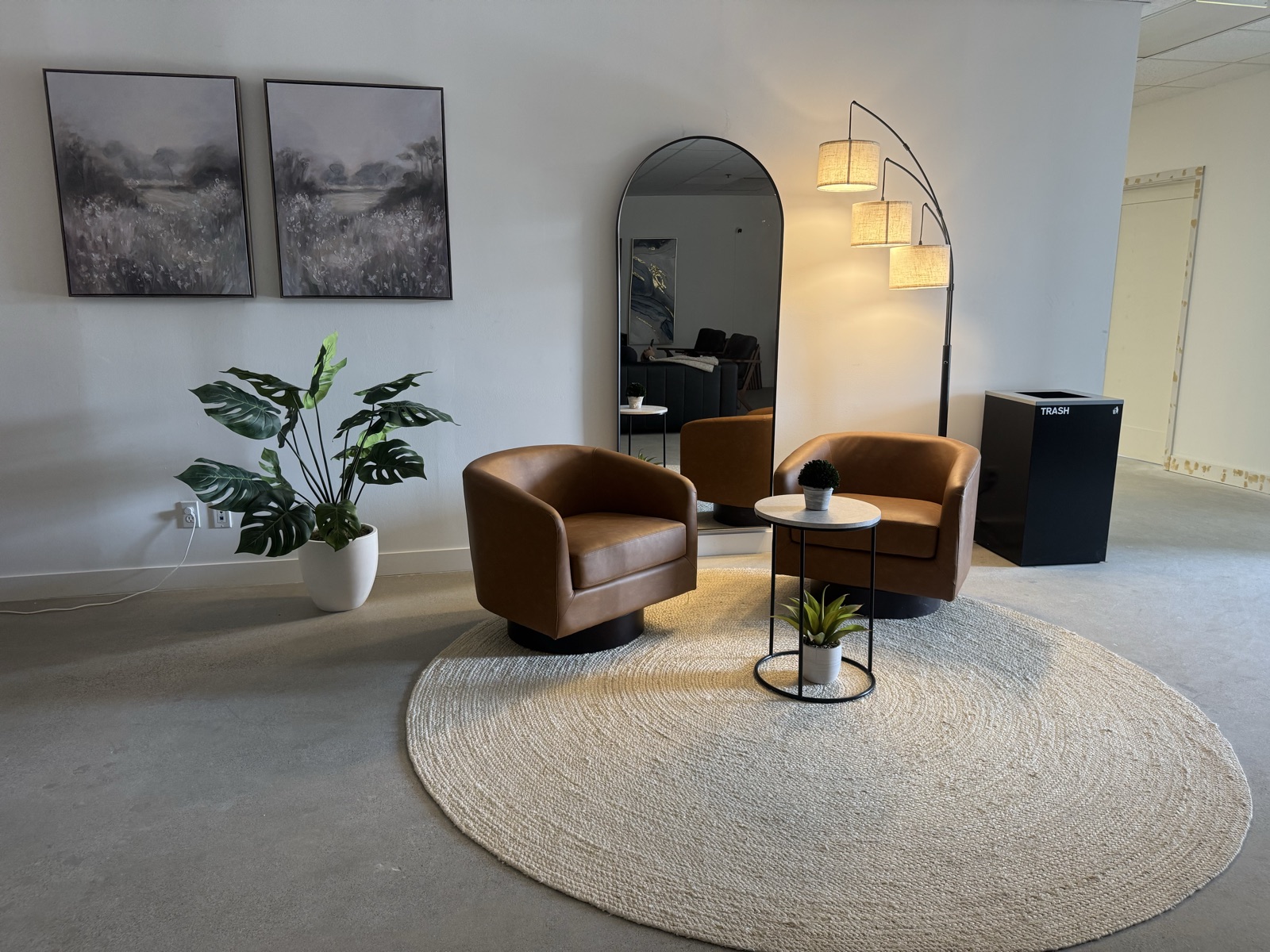 Waiting area with leather swivel chairs, round rug, and tall arched mirror